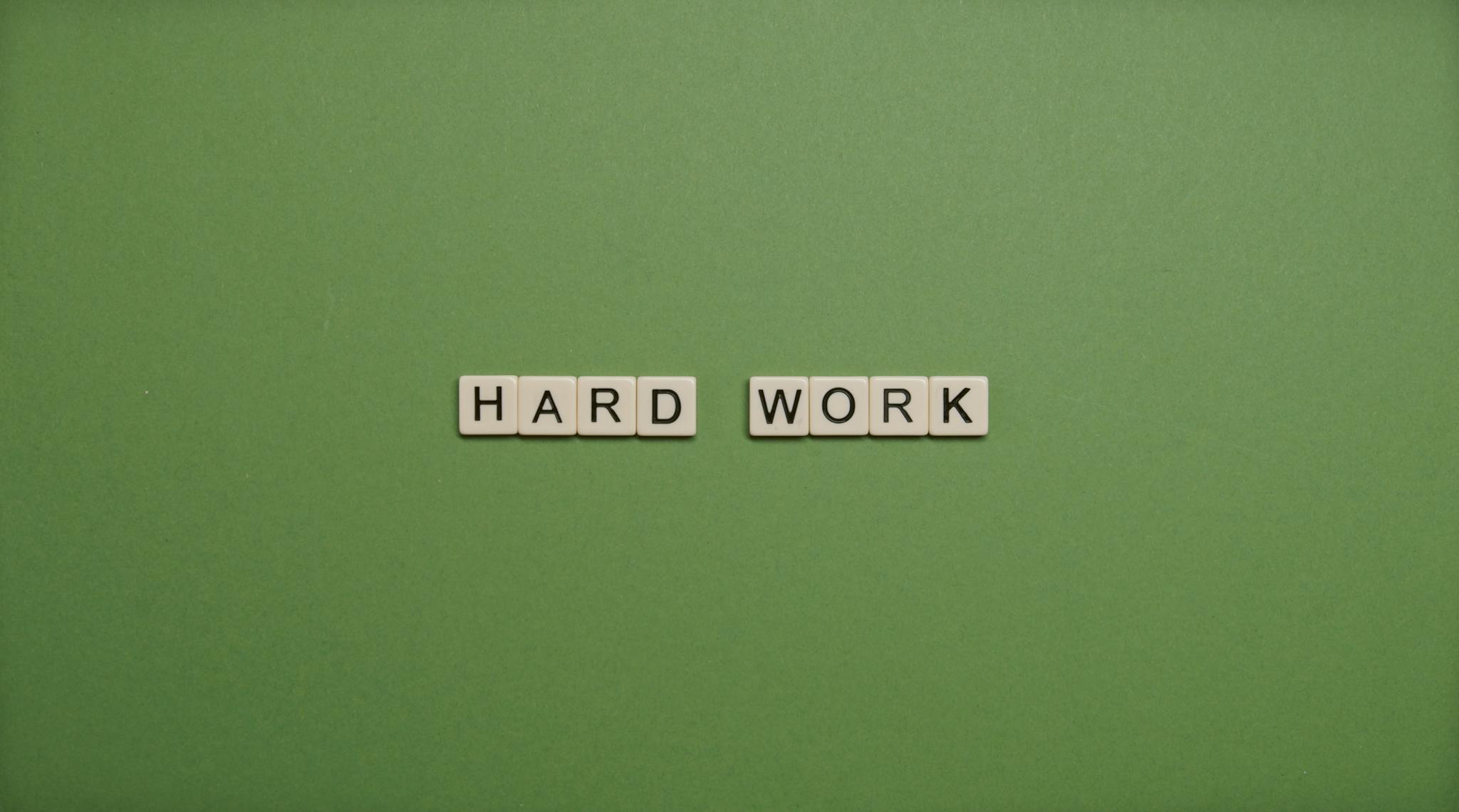 Tiles spelling 'hard work' on a green background symbolizing diligence and effort.